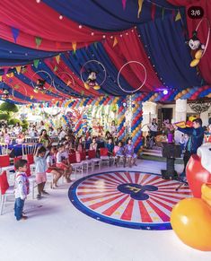 children are sitting in chairs under a circus tent with mickey mouse balloons and streamers