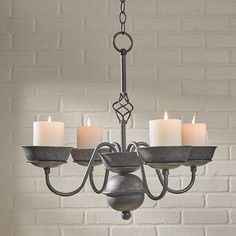 a chandelier with five lit candles in front of a white brick wall background