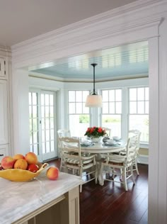 a bowl of fruit sitting on top of a kitchen counter next to a table with chairs