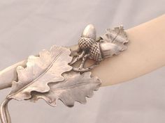 a silver bracelet with an oak leaf and acorns on it's arm