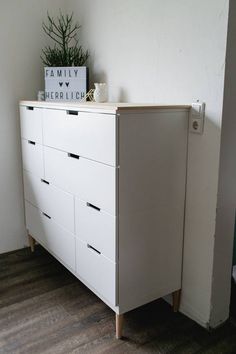 a white dresser sitting next to a wall with a potted plant on top of it