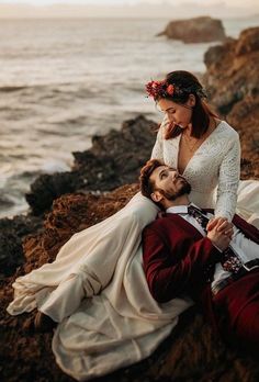 a man and woman are laying on the rocks by the ocean with their arms around each other