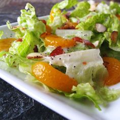 a salad with oranges and almonds on a square white plate, ready to be eaten