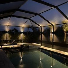 an indoor swimming pool at night with lights shining on the walls and ceiling, along with chaise lounges