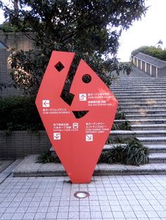 a large red sculpture sitting on the side of a cement walkway next to steps and trees