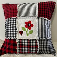 a red and black patchwork pillow with a flower on the front, two hearts in the back