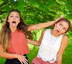 two women standing next to each other in front of a tree with their mouths open