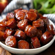 a white bowl filled with cooked sausage on top of a wooden table next to an apple