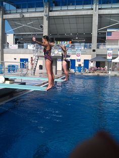 two women in bathing suits standing on the edge of a swimming pool while others watch