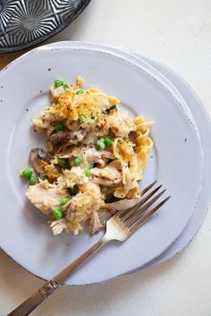 a white plate topped with pasta covered in chicken and peas next to a fork on top of a table