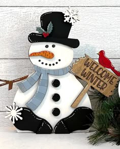 a snowman holding a welcome winter sign next to a christmas tree with a cardinal on it