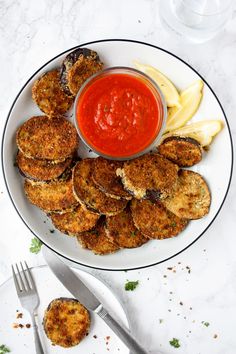 a white plate topped with fried food next to a bowl of sauce and silverware