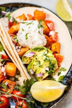 two tacos on a plate with tomatoes, avocado and sour cream