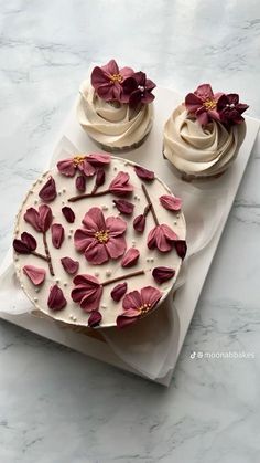 two cupcakes with white frosting and pink flowers on top sitting on a plate