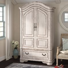 a white armoire sitting in a living room next to a chair