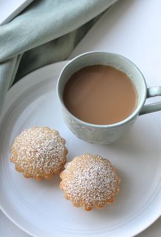 two powdered sugar cookies on a plate next to a cup of coffee