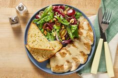 a blue plate topped with meat and salad next to two slices of bread on top of a wooden table