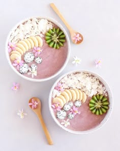 two bowls filled with rice and fruit on top of a white table next to spoons