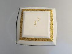 a white and gold square plate with an ornate design on the edge, sitting on a table