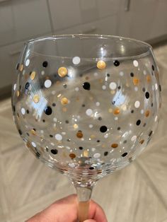 a hand holding a wine glass with gold and black dots on it