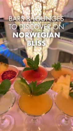 four glasses filled with different types of drinks on top of a white countertop next to a chandelier that reads bars & lounges to discovery norwegian bliss