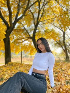 a woman sitting on the ground in front of trees with leaves all over her body