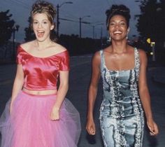 two women in dresses walking down the street at night, one wearing a pink and blue dress