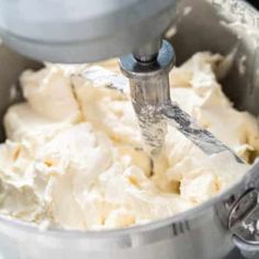 a mixing bowl filled with white batter and a mixer attachment in the middle of it