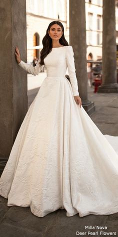 a woman in a white wedding dress leaning against a pillar with her hands on her hips