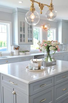 a kitchen island with flowers on it in front of two windows and lights hanging from the ceiling