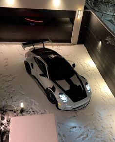 a white and black sports car parked in the snow next to a building with lights on