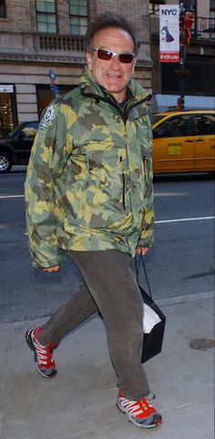 a man in camouflage jacket walking down the street with his handbag on his hip