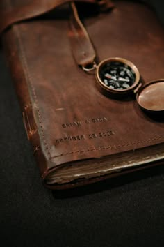 a brown leather book with a compass on the front and two other items in it