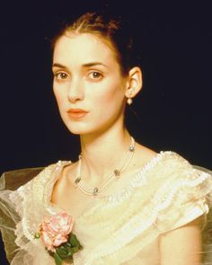 a woman in a white dress holding a pink rose and wearing pearls on her necklace