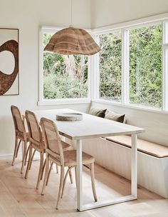 a dining room table with six chairs and a bench in front of large windows overlooking the woods