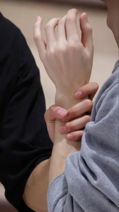 a person holding their hand on the wrist of another person who is wearing a gray shirt