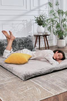 a woman laying on top of a bed in a living room next to a potted plant