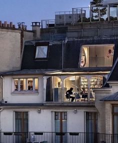 two people are standing on the balcony of a building at night with their windows open