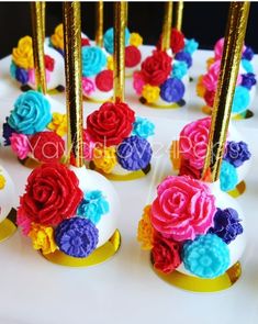 there are many colorful flowers on top of the cupcakes that have gold sticks sticking out of them