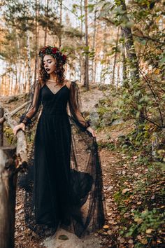 a woman in a black dress standing on a wooden bridge surrounded by trees and leaves