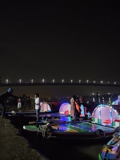 several people standing on small boats in the water at night with lights shining from them