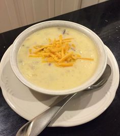 there is a bowl of soup with cheese on the top and spoon next to it