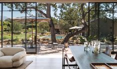 a living room filled with furniture next to a large glass window covered in plants and trees