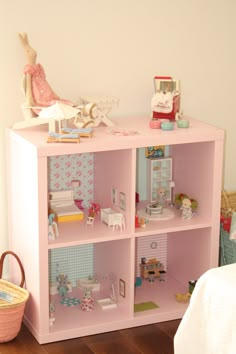 a pink shelf with dolls on top of it and a basket in the corner next to it