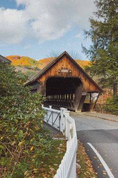 a wooden covered bridge over a river next to trees and bushes on the side of the road