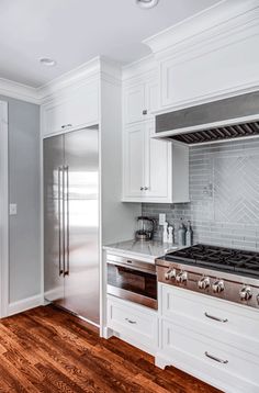 a kitchen with white cabinets and stainless steel stove top oven in the center of the room