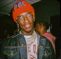 a man wearing a jean jacket and orange hat smiles at the camera while standing next to another man