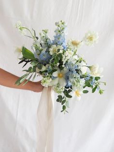 a bridal bouquet with blue and white flowers is held by someone's hand