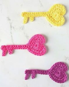 three crocheted keys are shown on a white surface, one is pink and the other is yellow