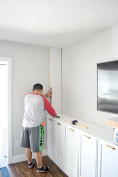 a man standing in front of a flat screen tv on top of a white wall